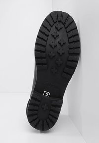 Semelle de botte en caoutchouc noire présentant un motif de semelle texturée avec des formes croisées. Comprend un logo de marque visible et la taille "5" imprimée.