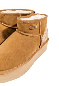 Botas de tobillo de ante en color marrón con un cómodo forro interior, que cuentan con una suela de goma suave y un acento metálico con el nombre de la marca.