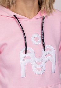 Różowa bluza z kapturem z bawełnianej mieszanki, z przodu z białym haftowanym wzorem oraz kontrastującymi czarnymi sznurkami z akcentami z logo.