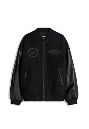 Zwarte bomberjas met contrasterende leren mouwen, ritszakken en sierlijke borduursels met de tekst "HOPELESSLY ADAPT" en andere ontwerpen.