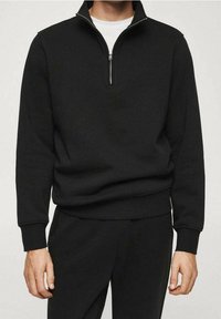 Maglione nero con collo a zip fino a un quarto, realizzato in tessuto strutturato. Caratterizzato da maniche lunghe con polsini a coste e vestibilità rilassata.