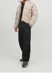 Ljusbeige puffjacka med dragkedja och ribbade manschetter, kombinerad med svarta byxor. Funktioner inkluderar en hög krage och minimal märkning.