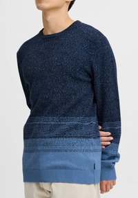 Marineblå strikkegenser med gradientmønster som går over til lyseblå, har rund hals og ribbestrikkede mansjetter og nederkant.