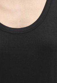 Κοντινή λήψη ενός μαύρου αμάνικου τοπ με στρογγυλή λαιμόκοψη που δείχνει την υφή του υφάσματος και τις ραφές σε ανοιχτόχρωμο δέρμα.