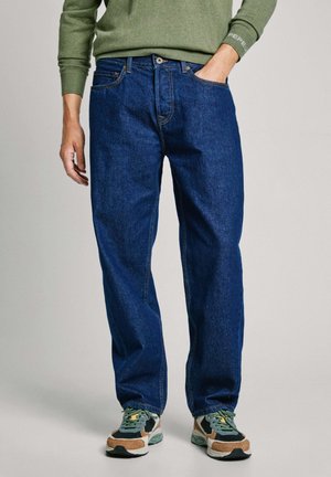 Jeans de denim azul con un corte relajado, que cuentan con bolsillos laterales y un cierre de botón, combinados con zapatillas deportivas multicolores.