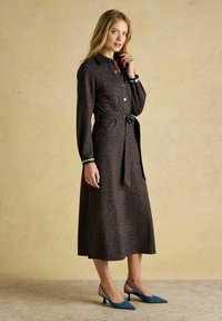 Gara brūna kleita ar tumšiem leoparda plankumiem, ar pogu priekšpusi un jostu viduklī. Iespējamās kontrastējošas svītraines piedurknes, kā arī valkāta ar zilām smailajām papēžkurpēm.