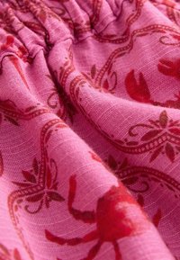Tissu rose avec des motifs floraux rouges et paisley, montrant une texture détaillée et des plis.