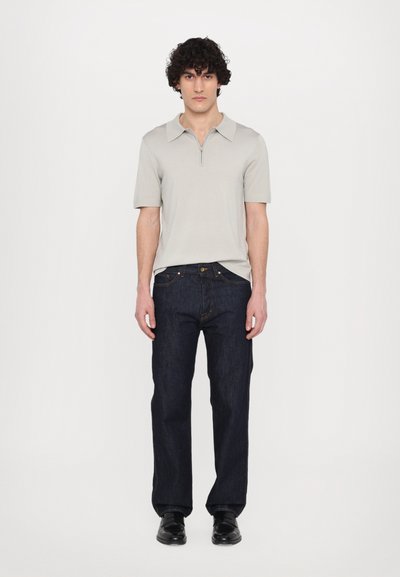 Polo grigio chiaro a maniche corte con zip, abbinato a jeans dritti blu scuro e scarpe nere. Texture liscia e design moderno.
