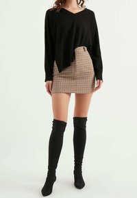 Top nero a maniche lunghe con scollo a V, abbinato a una minigonna beige con fantasia e stivali neri sopra il ginocchio. Texture lisce visibili.