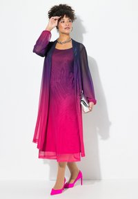 Lång gradientklänning som övergår från lila till rosa, med genomskinlig överdel, långa ärmar, i kombination med rosa högklackade skor och en silverfärgad clutch.