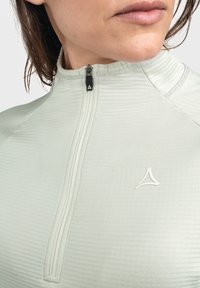 Hellgrünes sportliches Quarter-Zip-Oberteil mit gerippter Textur, einem hohen Kragen und einem kleinen weißen Logo auf der Brust. Der Reißverschluss verfügt über einen schwarzen Ziehgriff.