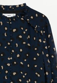 Blouse marine avec imprimé léopard beige et noir, col à volants, boutons recouverts de tissu sur le devant, et manches longues en tissu transparent.