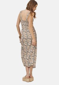 Vestido maxi sin mangas con estampado floral y espalda fruncida. Presenta una silueta fluida y un tejido suave y ligero en tonos beige y azul.
