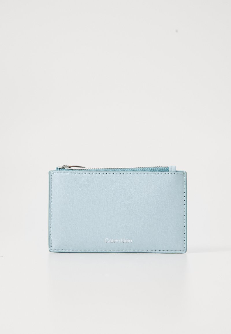 Carteira de pele azul clara com fecho de zip, forma retangular e bordas cosidas. Apresenta um logótipo prateado na frente.