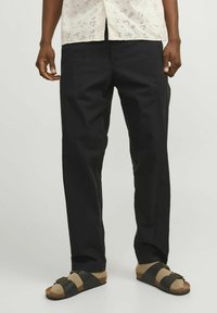 Pantalones negros de pierna recta hechos de algodón, combinados con sandalias marrones y negras. La parte superior presenta un diseño ligero y perforado.