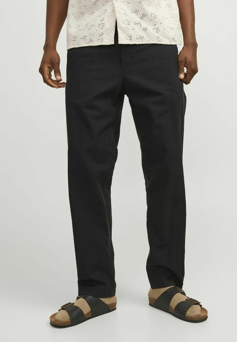 Pantalones negros de pierna recta hechos de algodón, combinados con sandalias marrones y negras. La parte superior presenta un diseño ligero y perforado.