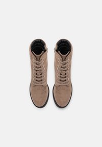Botas de tobillo de ante marrón con cordones en la parte delantera, ojetes plateados y interior acolchado. Suela plana de goma negra. Cremallera en el lado exterior.