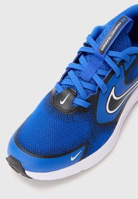 La scarpa da corsa Nike presenta una tomaia in mesh blu, accenti neri, il classico swoosh Nike bianco e lacci piatti, progettata per traspirabilità e comfort.
