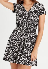 Robe noire à motifs floraux, avec un décolleté en V, des manches courtes, une taille cintrée et une jupe évasée ornée de motifs de fleurs blanches.