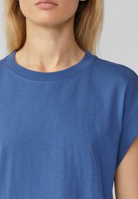 Blaues Baumwoll-T-Shirt mit Rundhalsausschnitt, kurzen Ärmeln und einer glatten Textur mit feinen Rippungen am Kragen.
