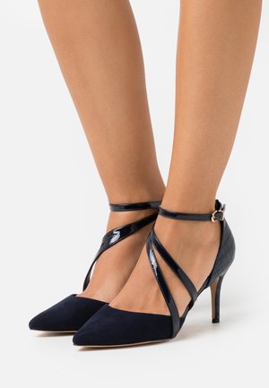 Granatowe szpilki z wąskim noskiem, wykonane z zamszu i lakierowanej skóry. Posiadają krzyżujące się paski na kostce oraz cienką szpilkę. Teksturowany wzór obcasa.