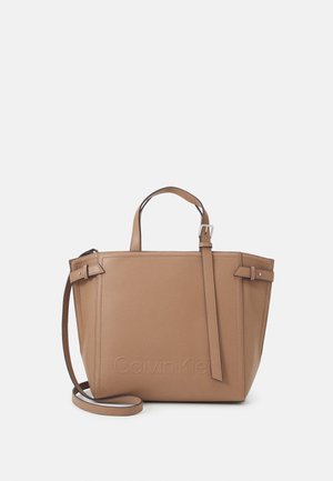 Tan leather handbag with dual handles and an adjustable strap. Features a rectangular shape, embossed branding, and minimalistic design.