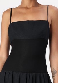 Μαύρο φόρεμα με εφαρμοστό μπούστο, μαλακή υφή, λεπτές τιράντες και φουσκωτό, ριγέ φουστάνι από αντίθετο ύφασμα.