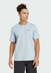 Svetlomodré tričko s krátkym rukávom vyrobené z jemnej textílie, s malým sivým logom "Terrex" na ľavej hrudi a klasickým okrúhlym výstrihom.