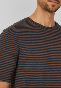 Camiseta a rayas con líneas horizontales en tonos azul marino y óxido. Cuello redondo y mangas cortas, fabricada en un tejido suave y texturizado.