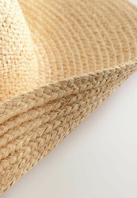Cappello di paglia intrecciato con una larga visiera, di colore beige naturale e una superficie texture creata da intricati schemi di intreccio.