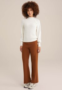 Balta šonkaine mezgimo megztinis su šoninėmis mygtukų detalėmis, derinamas su rudomis plačiomis kelnėmis. Alyvuogių spalvos sportbačiai su pilkomis detalėmis puikiai užbaigia įvaizdį.