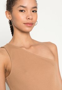 Bodysuit castanho com um ombro, feito de material suave, apresentando um design ajustado e textura lisa. Brincos de argola prateados como acessório.