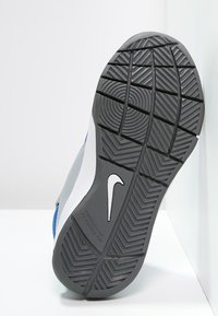 Szara gumowa podeszwa z teksturowanym wzorem, z białym logo Nike i niebieskimi akcentami, prezentująca wzór bieżnika, który nie brudzi.