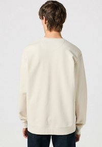 Felpa beige con collo rotondo, polsini e orlo a costine. Tessuto liscio, design semplice e vestibilità leggermente oversize. Vista posteriore visualizzata.