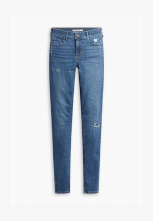 Jean en denim bleu avec une coupe slim, présentant des détails déchirés, un léger délavage et une fermeture à bouton classique, conçu pour un usage décontracté.