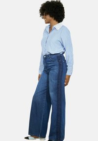 Blauw-wit gestreept overhemdd met een kantenkraag, gecombineerd met hoge taille, wijde denim jeans met een contrasterende zijpaneel.