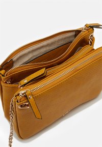 Borsa color giallo senape con un esterno testurizzato, dotata di diversi scomparti con zip, hardware in tonalità oro e una tracolla a catena removibile.