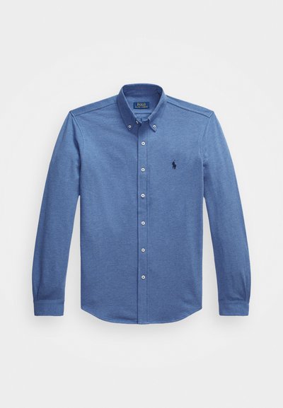 Camisa azul de manga longa, com botões, feita de um tecido de mistura de algodão. Apresenta um colarinho pontudo, fechamento com cinco botões e um pequeno logótipo bordado no peito.