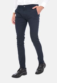 Pantaloni blu slim-fit realizzati in un tessuto morbido, con tasche anteriori, un bottone e un design minimalista, abbinati a scarpe eleganti nere.