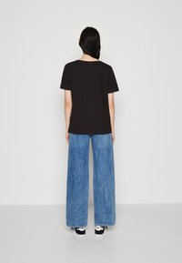 Sort kortærmet t-shirt parret med lys blå brede jeans og sorte sneakers, set fra ryggen mod en hvid baggrund.