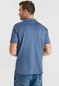 Polo blu navy con maniche corte, dalla texture morbida, e un piccolo accento con la bandiera francese sul colletto. Indossato con jeans in denim.