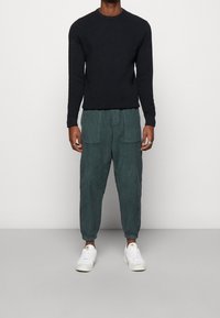 Černé pletené tričko s dlouhým rukávem v kombinaci s volnými tyrkysovými manšestráky a bílými teniskami. Kalhoty mají boční kapsy a elastické manžety.