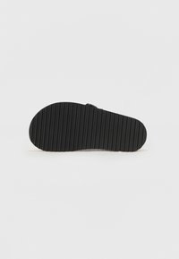 Semelle de chaussure en caoutchouc noir présentant un motif texturé et rainuré. Sa forme est allongée avec des bords arrondis et une surface lisse.
