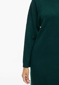 Adīta džemperkleita tumši zaļā krāsā, ar garām piedurknēm, brīvu piegriezumu un ribotām aprocēm. Mīksta tekstūra ar vieglu spīdumu.