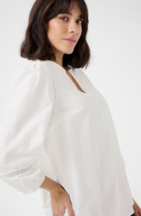 White blouse with a keyhole neckline, puffed sleeves, and lace trim at the cuffs. Made from lightweight fabric, smooth texture.