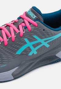 Scarpa da ginnastica grigia con lacci rosa, caratterizzata da un design superiore testurizzato e dettagli blu. La suola presenta il marchio "WINGWALL".