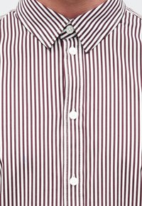Camisa a rayas granate y blancas con cuello, seis botones y costuras en contraste a lo largo de la tapeta y los puños.