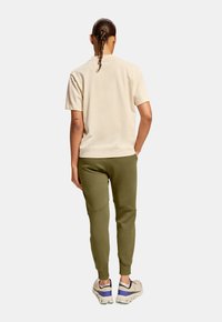 Beige kortærmet skjorte parret med olivengrønne joggers. Joggers har en tapered design og ribbede manchetter. Fodtøjet er neutralt med lilla accenter.