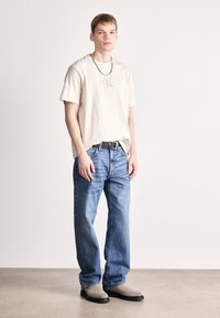 Μπεζ βαμβακερό T-shirt με λογότυπο CK, μπλε τζιν παντελόνι, γκρίζες μπότες μέχρι τον αστράγαλο και ασημένια αλυσίδα. Απλό, χαλαρό στυλ και μίνιμαλ σχέδιο.