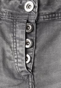 Tela de mezclilla gris con un acabado texturizado, que presenta botones metálicos plateados en la parte delantera. El diseño incluye una costura lateral y costuras visibles.